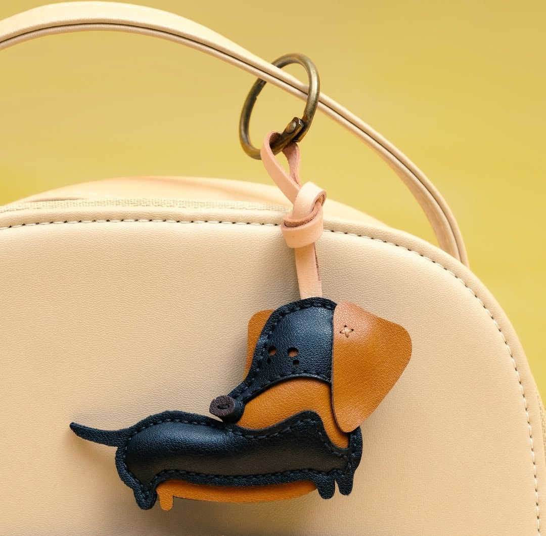 Leather dachshund keychain attached to a beige handbag against a yellow background