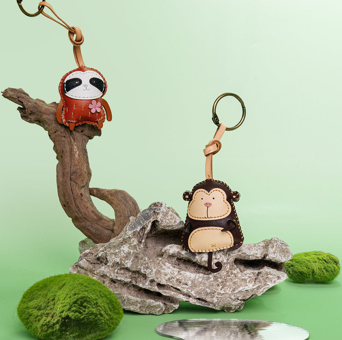 Two monkey-themed keychains on a natural background with greenery.
