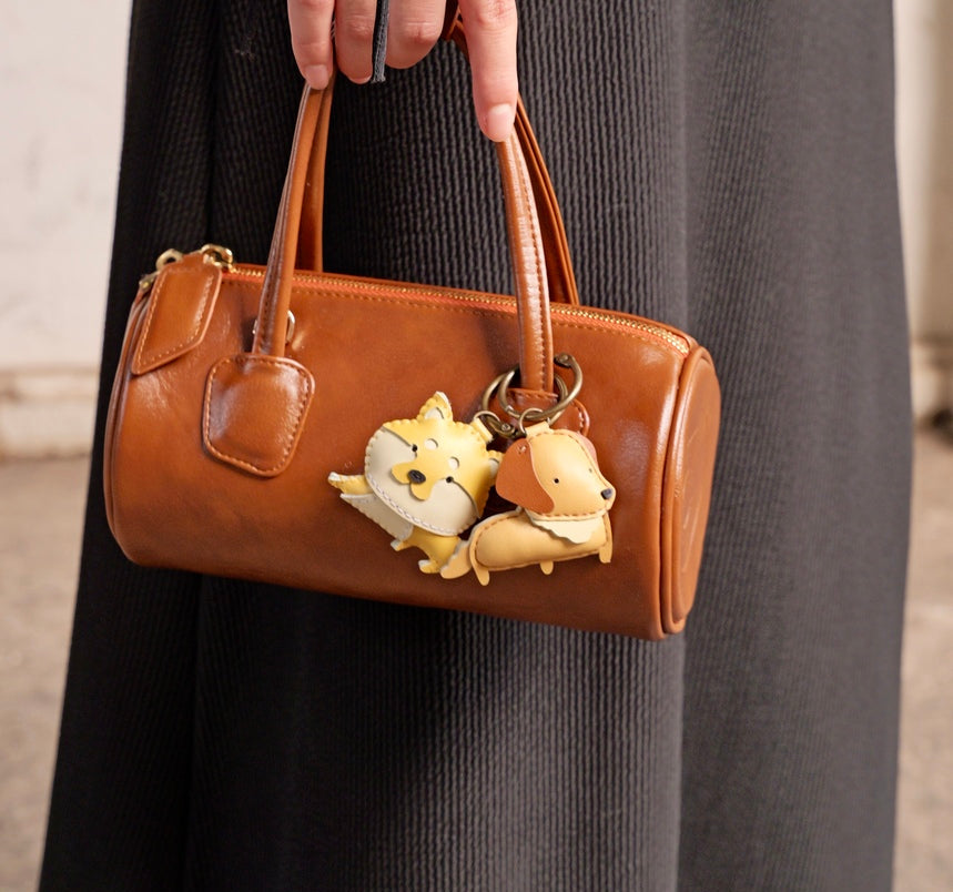 Brown handbag with dog-shaped keychains held by a person wearing a dark coat.