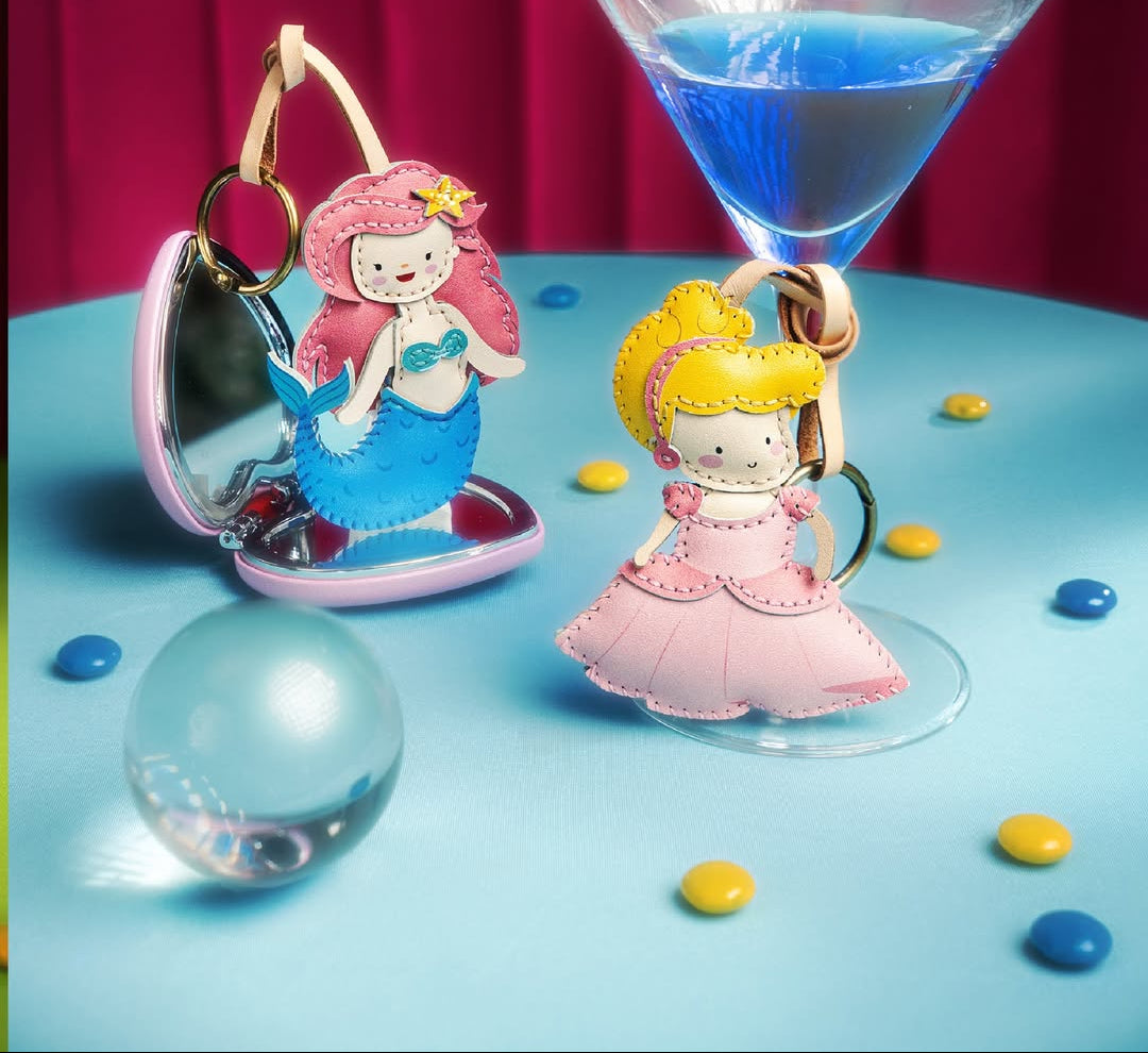 Mermaid-themed keychains with a glass of blue liquid on a blue surface.