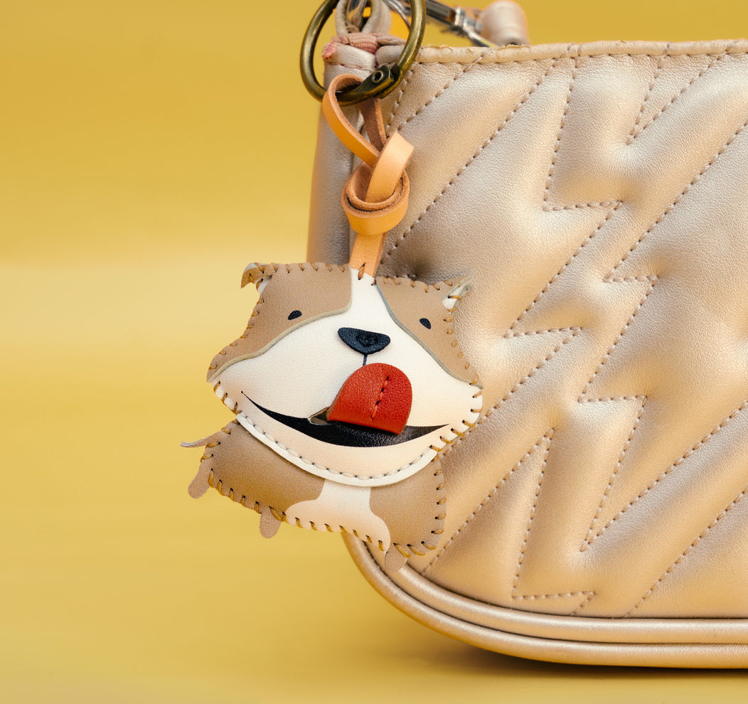 Dog-shaped keychain attached to a beige quilted handbag on a yellow background